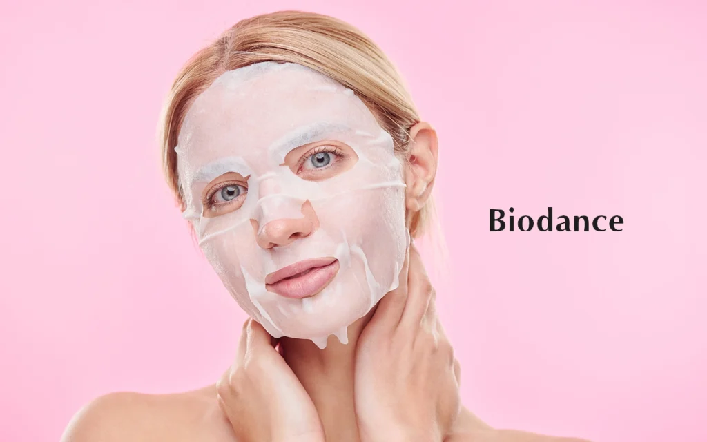 a blonde girl with grey eye wearing biodance face mask for her daiy routine skincare in close up picture with pink background